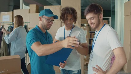 Male Volunteers at White T Shirts Talking With Mentor at Volunteer Warehouse. Charity, Donation, and Volunteering Concept. Work of the Volunteer Center