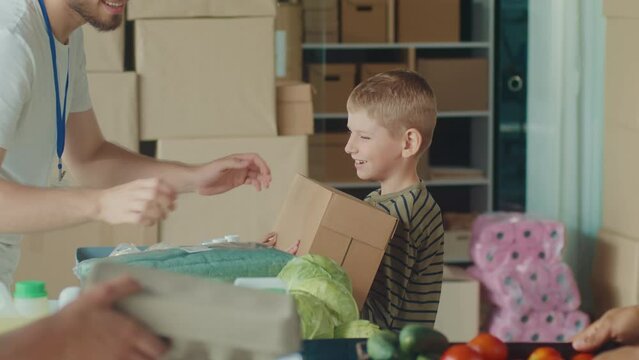 The Concept of Social Aid: A Child in a Volunteer Center Receives a Box of Food from Friendly Volunteer at at Distribution or Refugee Assistance Center.