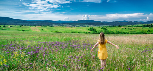 Naklejka na ściany i meble Woman in yellow dress staying at the green meadow in the mountain