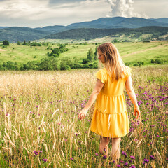 Woman in yellow dress staying at the green meadow in the mountain