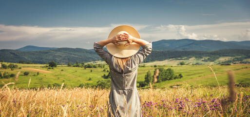 Woman in dress and hat staying at the green meadow in the mountain