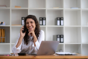 Young smiling business woman using smartphone near computer in office, copy space