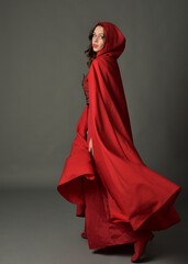 Full length portrait of woman wearing red medieval fantasy costume, flowing hooded cloak. Standing...