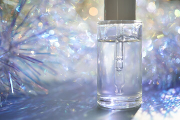 A bottle of serum with a pipette in tinsel in a Christmas theme in purple shades.