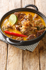 Spicy goat curry with coconut milk and spices close-up in a frying pan on the table. Vertical