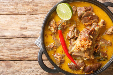 Gulai Kambing traditional Javanese mutton curry stew closeup on the pan on the wooden table. Horizontal top view from above