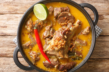 Gulai Kambing or Indonesian Traditional Delicious Goat Curry closeup on the pan on the wooden table. Horizontal top view from above