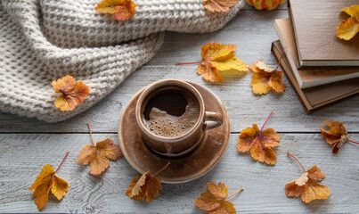Autumn mood, autumn atmosphere. A cup of coffee, a knitted scarf, books and autumn leaves on the windowsill.