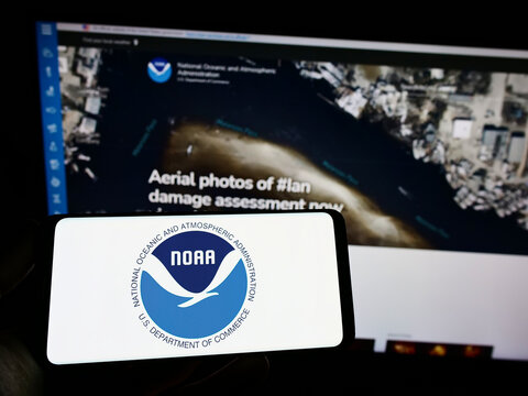 Stuttgart, Germany - 10-09-2022: Person holding smartphone with logo of National Oceanic and Atmospheric Administration (NOAA) on screen with web page. Focus on phone display.