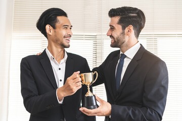 Good job of achievement, happy success asian young businessman, man employee holding golden trophy cup, team getting rewarded for winning from caucasian man boss. Celebration of Teamwork of business.