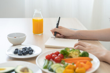 Obraz na płótnie Canvas Diet, Dieting hand of asian young woman, girl write diet plan nutrition on table is different food ingredients in the green. Nutritionist of healthy, nutrition of weight loss, health care people.
