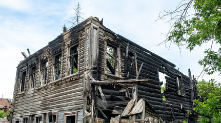 Burnt house on a city street in Russia. Wooden building after the fire. Remains of a residential building after a fire incident. Sunny day. Summer.