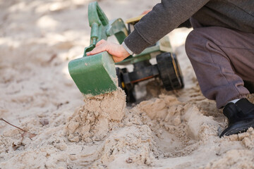 Preschool child playing in sandbox with green digger at kindergarten