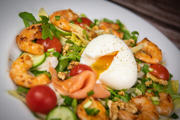 Recipe for rocket salad, endive, tomato, cucumber, soft-boiled egg, fried shrimp with paprika, smoked salmon and nuts. High quality photo