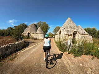 Back shot of an adult woman riding a bicycle on a lane through old trulli houses in Puglia, Italy