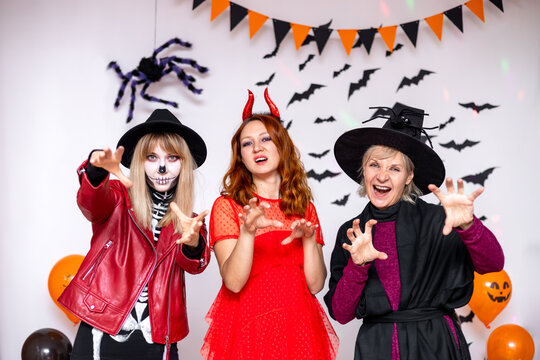 three women in carnival costumes of a skeleton, a witch and a devil. halloween party