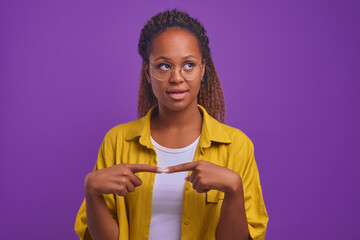 Young beautiful curly African American woman shyly looks up and connects fingers in front of chest...