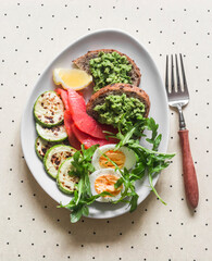 Delicious breakfast, snack - boiled egg, smoked salmon, grilled zucchini, avocado toast on a light background, top view