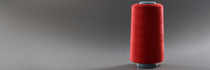 Red colour thread spool on grey background, yarn for sewing, bright thread for dressmaking