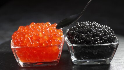 Red and black caviar in two identical transparent glass bowls on a black background. Man spoons...