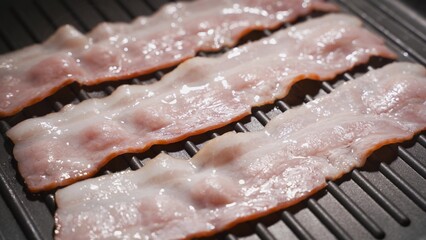 Strips of bacon are fried in a pan. Close-up, partial focus