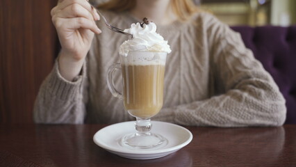 A girl takes a cream from coffee using a spoon