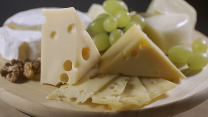 Cheese plate with grapes, honey and nuts rotating on gray background