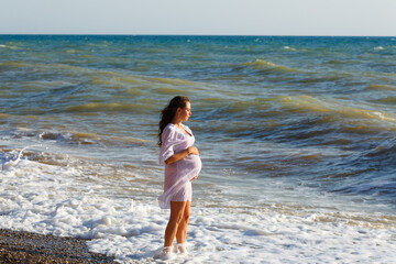 Fototapeta na wymiar Portrait beautiful young pregnant woman, against blue sea on beach, thoughtful and serene on the sunny coast, outdoor figure. Healthy Pregnancy Activities, Leisure Wellness Lifestyle
