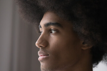 Obraz premium Serious or concerned African hipster guy with curly hair staring aside standing indoors, looking into distance thinking, deep in thoughts. Generation Z person, natural beauty, pensive mood, memories