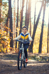 Fototapeta premium Happy kid boy having fun in autumn forest with a bicycle on beautiful fall day.