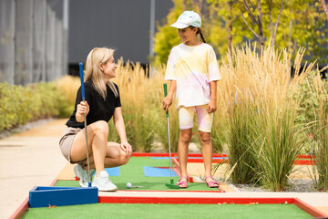 Mother playing with her cute daughter mini golf at outdoor playground.