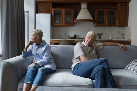 Older silent couple after quarrel sit on sofa apart, not talking, feeling annoyance, looking frustrated due to misunderstanding, lack of understanding between spouses. Family conflict, marital crisis
