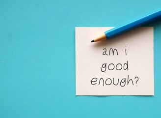 On copy space blue background, pen and note AM I GOOD ENOUGH? - negative self talk showing self...