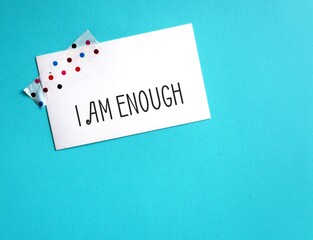 Stick note on blue copy space background with handwritten text I AM ENOUGH, Positive mantra...