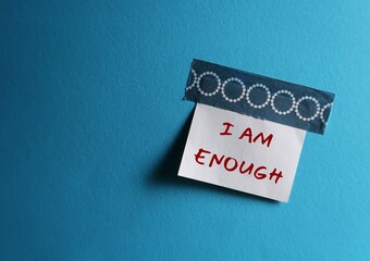 Fototapeta na wymiar Stick note on blue copy space background with handwritten text I AM ENOUGH concept of self-acceptance, affirmation to tell yourself you are capable enough to become everything you want to be