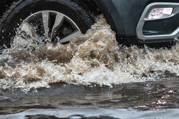 The car is driving through a puddle in heavy rain. Splashes of water from under the wheels of a car. Flooding and high water in the city.