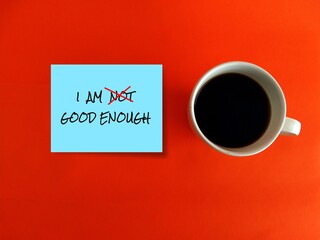 Coffee cup and blue note with text written I AM NOT GOOD ENOUGH with red cross on NOT, an aspiration motivation self talk to boost self esteem ,encourage self-worth.