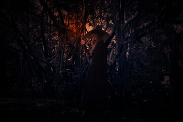 Halloween witch holding magic wand standing over spooky dark forest with tree, leaves and vine,...