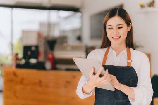 Opening A Small Business, AHappy Asian Woman In An Apron Standing Near A Bar Counter Coffee Shop, Small Business Owner, Restaurant, Barista, Cafe, Online, SME, Entrepreneur, And Seller Concept