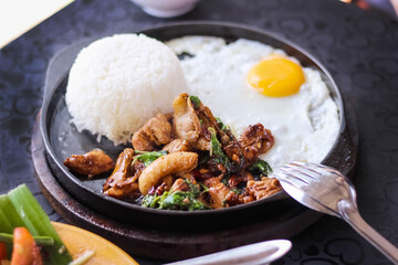 
Stir fried chicken with thai basil ,rice and fried egg  (Khao pad krapow) in black hot pan on table food background