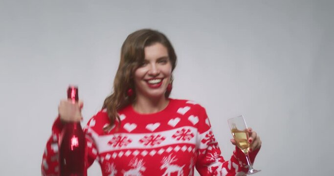Woman raising glass of champagne and dancing on party with sparkler, dressed in christmas sweater isolated on white background