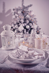 Festive  Christmas table place setting with silverware, candles and decorated Christmas tree