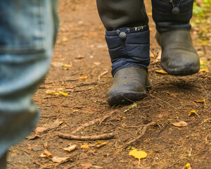 the legs of an adult dressed in warm old boots for traveling, walking through a green forest.