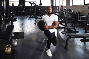Fototapeta na wymiar Handsome african man is working out with dumbbells at gym.