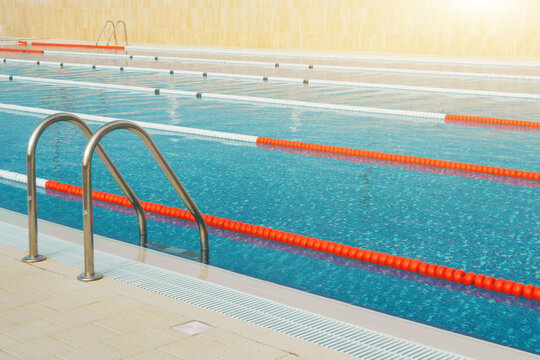 Swimming pool with divided lanes for competition and training and a ladder for going out and diving in the open air, illuminated by the bright sun