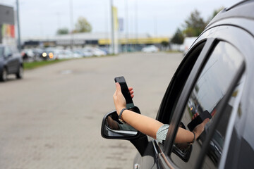 Telefon w dłoni kobiety wysuniętej przez okno samochodu osobowego, suwa, na placu przed marketem.