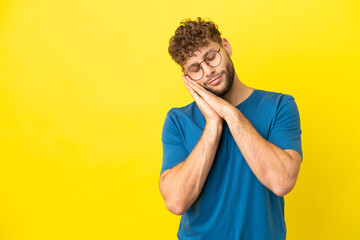 Young handsome caucasian man isolated on yellow background making sleep gesture in dorable expression