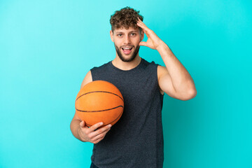 Handsome young man playing basketball isolated on blue background with surprise expression