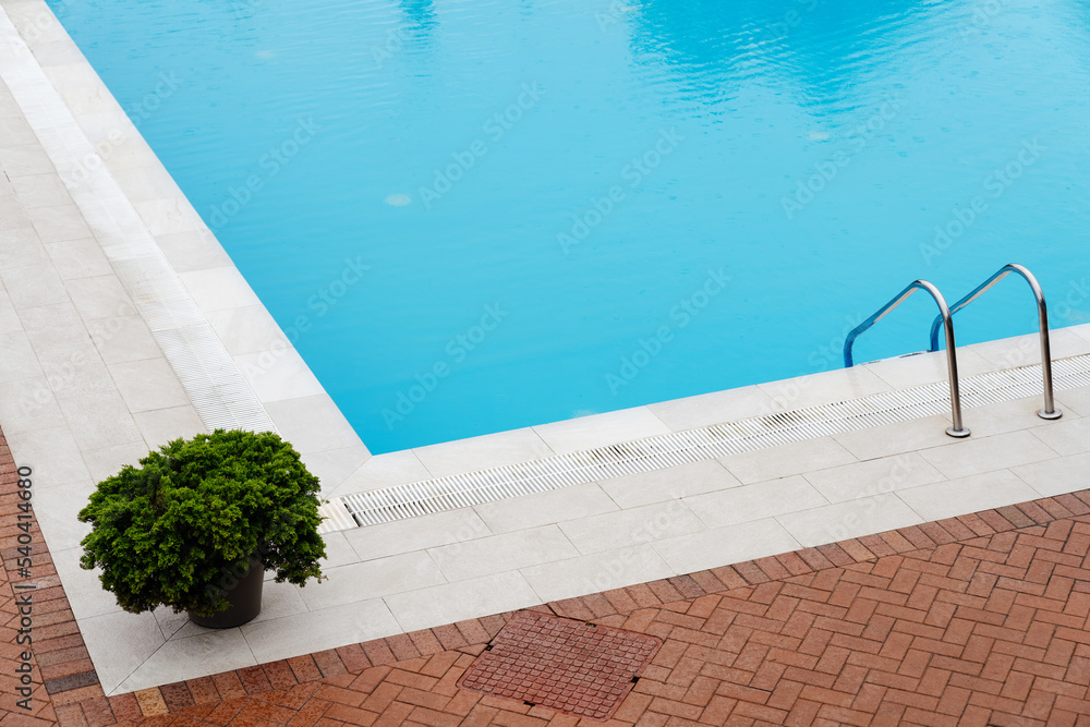 Wall mural The concept of summer holidays and architecture. Blue swimming pool in the rain with elements of greenery.