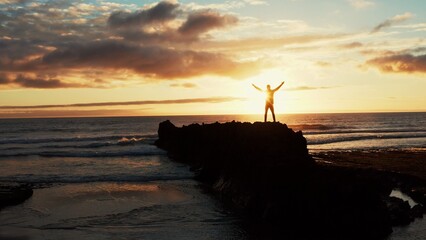 Human with raised hands looks to the sun over horizon in morning while sunrise.  Man stands on a...